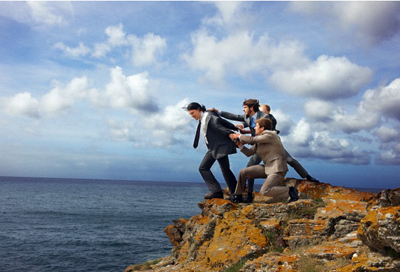 Businessmen pulling colleague from cliff